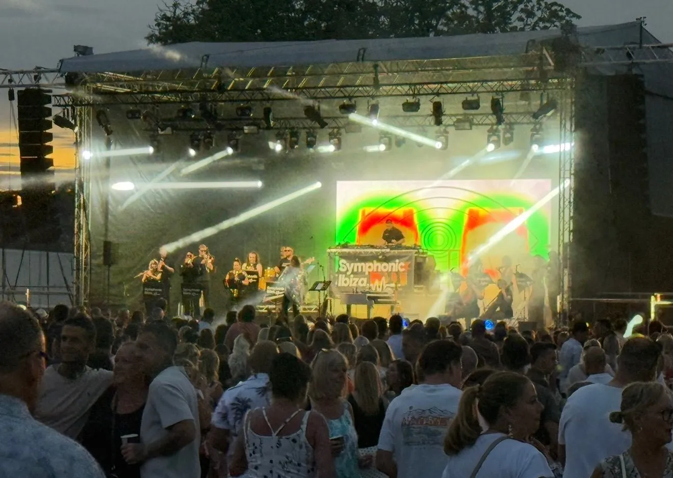Audience gathered in front of a stage with bright beams and colourful lighting