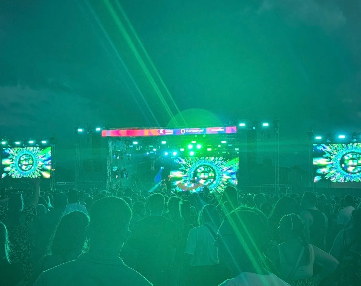Large audience facing a colourful outdoor stage and festival tent