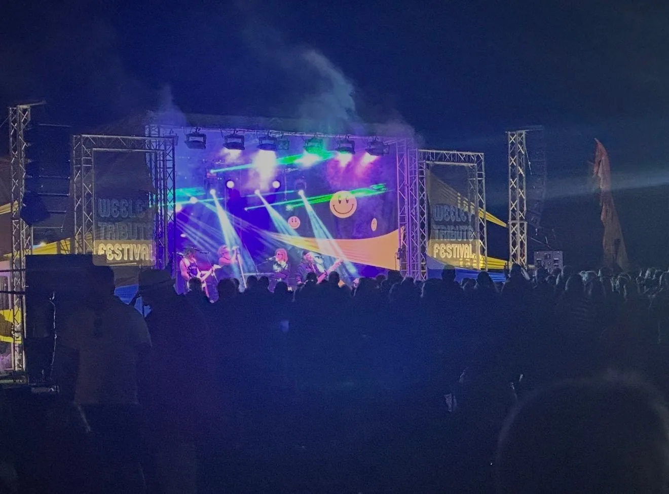 Crowd gathered beneath a dark sky in front of a colourful lit festival stage