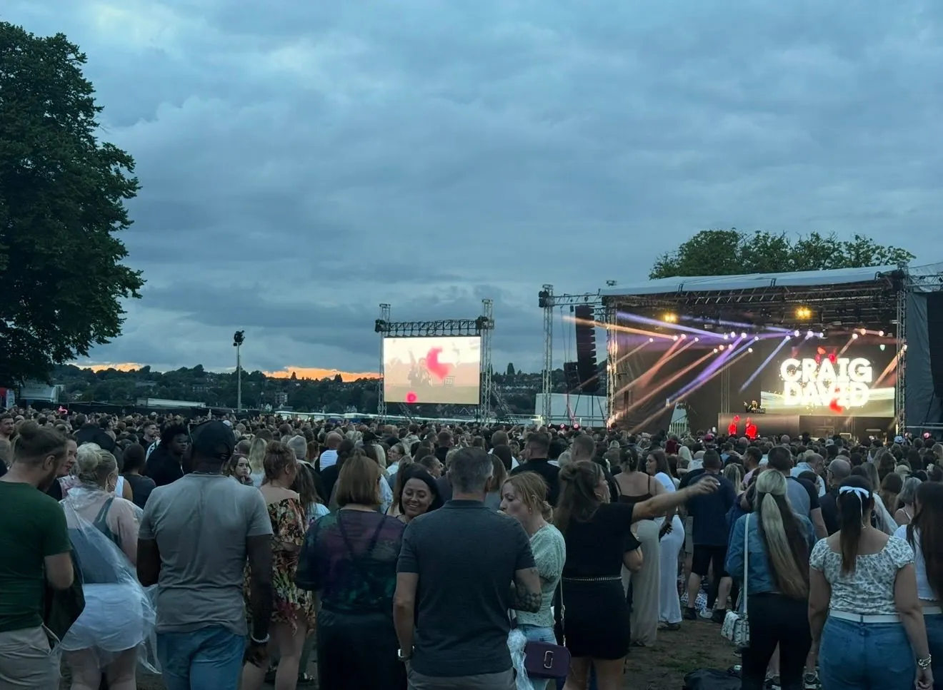 Large crowd watching an outdoor stage as evening falls